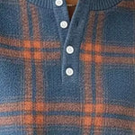 Close-up of a blue knit henley sweater with an orange plaid pattern and white buttons.