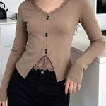 A woman wearing a beige long-sleeve cardigan with a button-up front, lace trim at the neckline, and a split hem, paired with black pants in a modern kitchen setting.