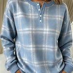 A woman wearing a light blue and white plaid long-sleeve henley sweater with a three-button placket, paired with white pants.