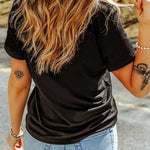Person wearing a black t-shirt and light blue jeans with tattoos on arms outdoors.