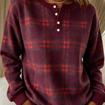 A woman wearing a long-sleeve henley sweatshirt in a dark burgundy and red plaid pattern, paired with white pants.