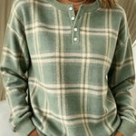 A woman wearing a sage green and cream plaid long-sleeve henley sweater with white buttons, paired with white pants.