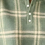 Close-up of a green and cream plaid knit henley top with a ribbed crew neck and three white buttons.
