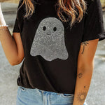 A woman wearing a black short-sleeve t-shirt with a sparkling ghost graphic on the front, paired with light blue jeans, photographed outdoors.