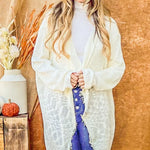 Woman wearing a white cardigan and blue jeans with a blue hat, standing against a wooden background.