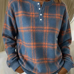A woman wearing a blue and orange plaid long-sleeve henley sweater with white buttons, paired with white pants.