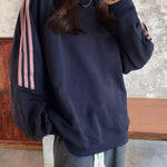 A person wearing a navy blue sweatshirt with three pink stripes down the sleeves, paired with gray drawstring sweatpants, taking a mirror selfie.