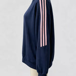 A navy blue crewneck sweatshirt with three pink stripes down the sleeve, displayed on a cream mannequin torso against a light gray background.